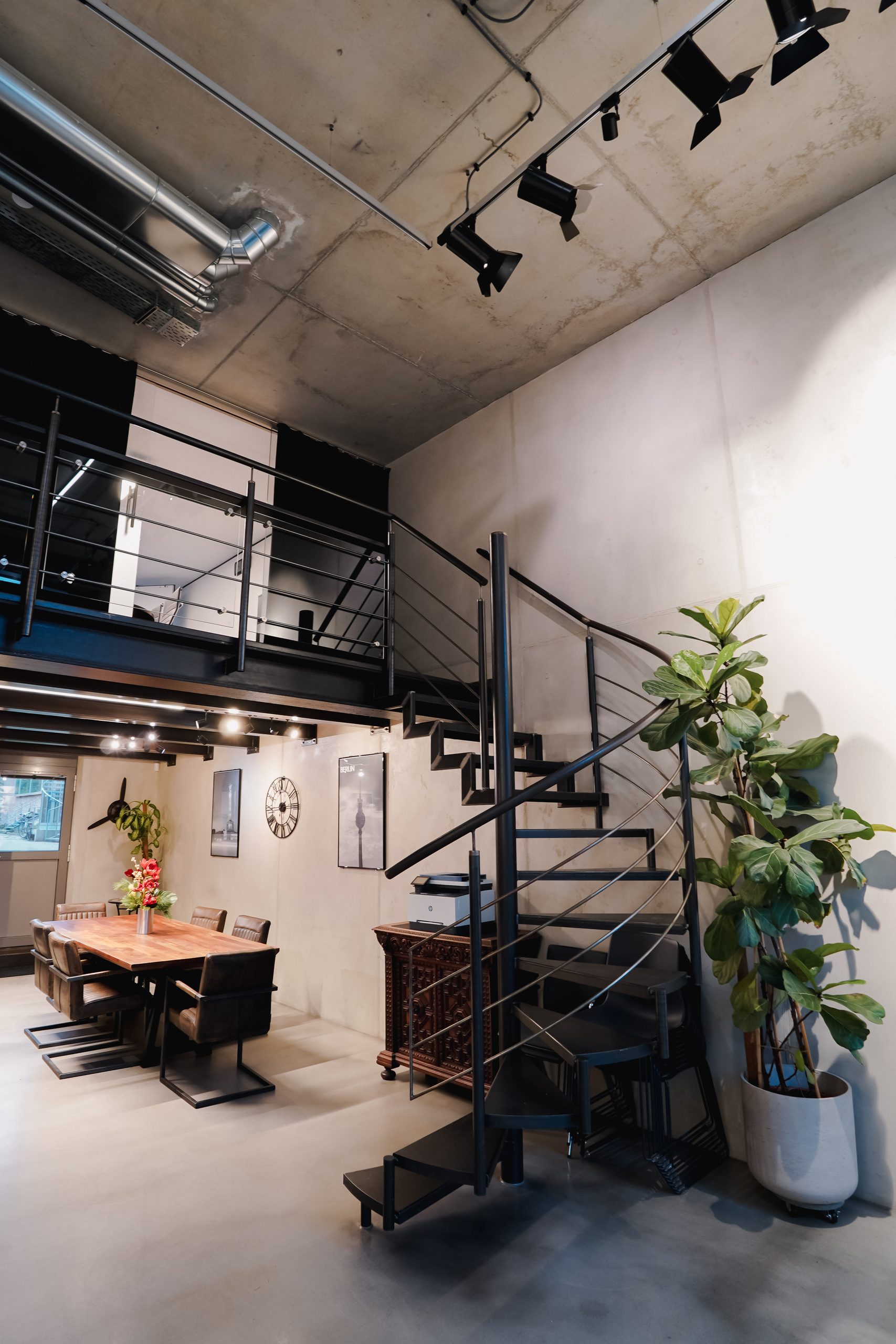 Work area with wooden table under the gallery, spiral staircase and large plant