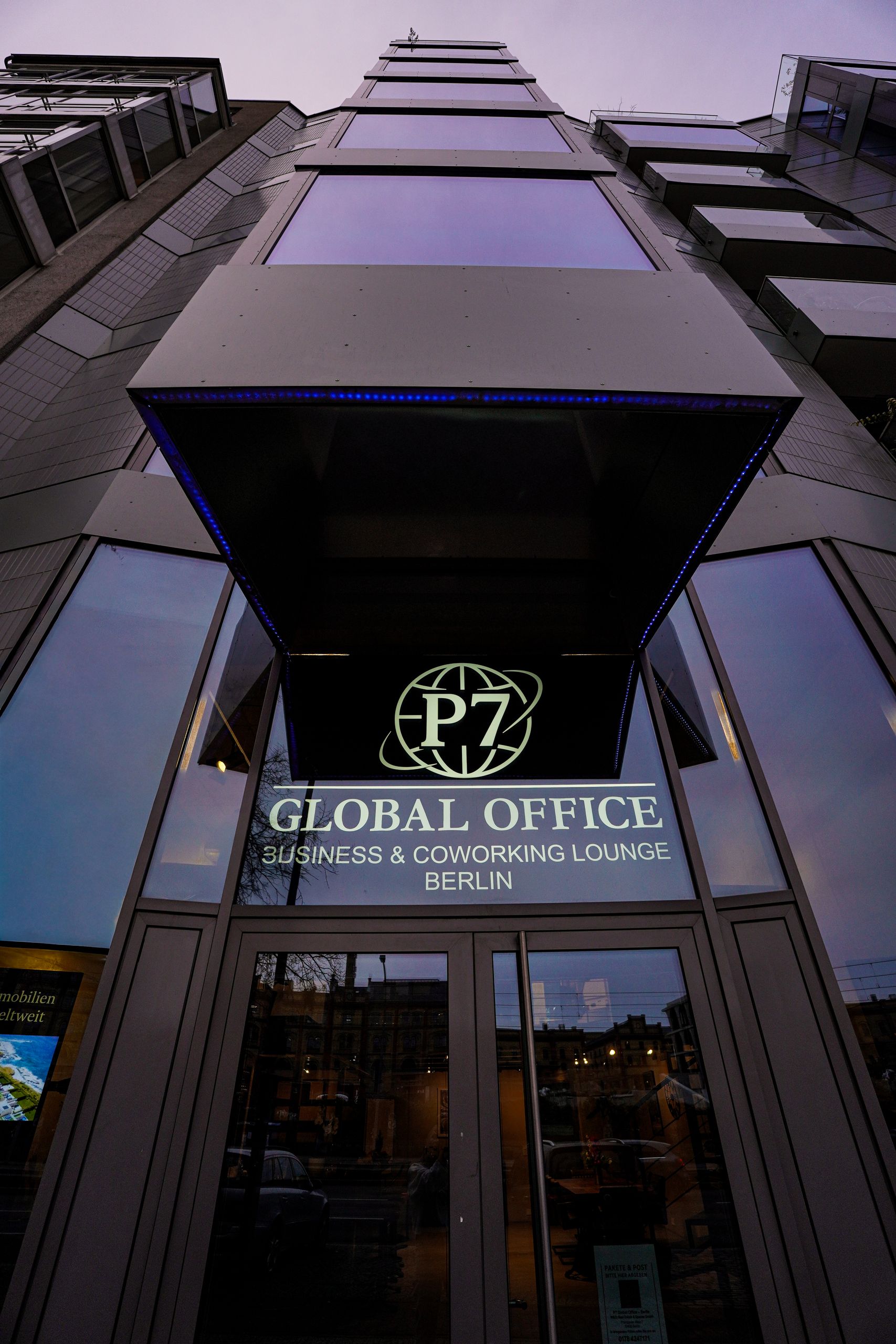 Eingang des P7 Global Office mit beleuchtetem Logo am Abend, Blick an der Fassade nach oben